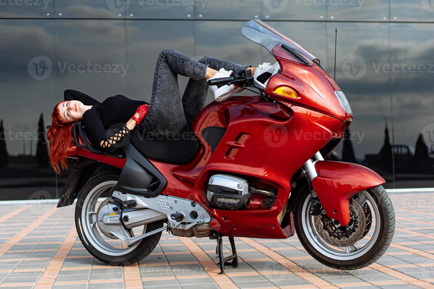 femme repos sur rouge moto. une femme confortablement mensonge sur Haut de une vibrant rouge moto. photo