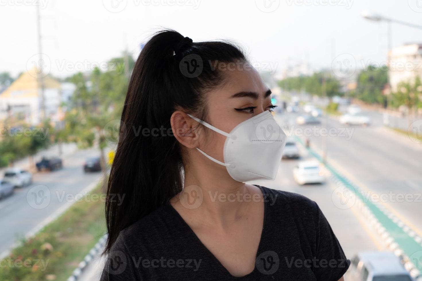 gros plan d'une femme debout mettant un masque respiratoire n95 pour se protéger des maladies respiratoires aéroportées comme la grippe covid-19 coronavirus ebola pm2.5 poussière et smog sur la route arrière-plan bavure photo