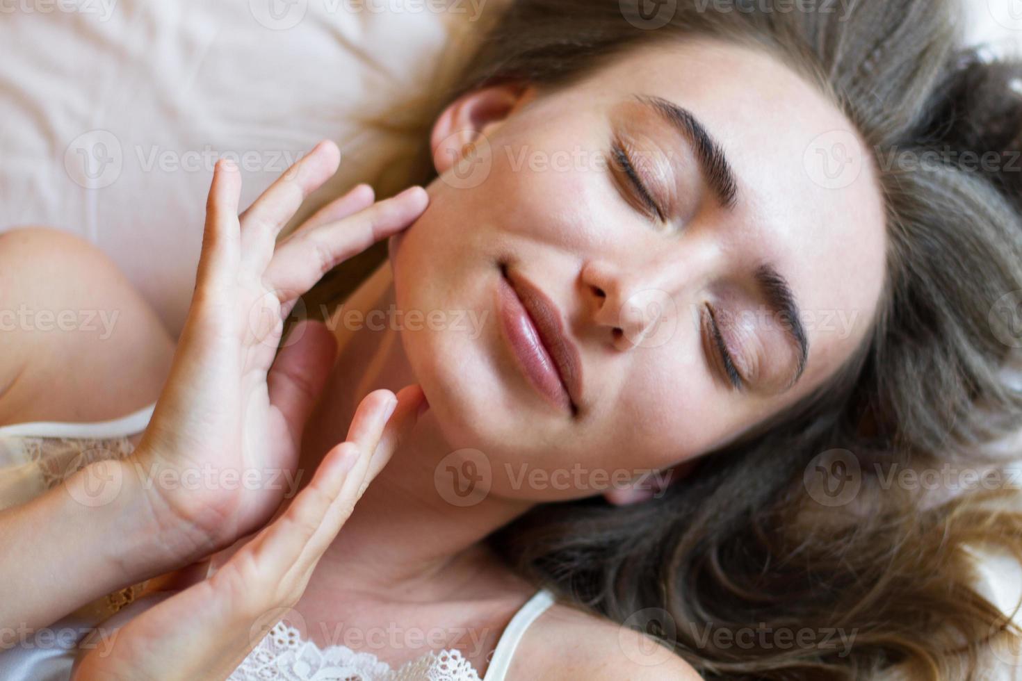 la dame endormie est allongée dans son lit les yeux fermés et touche son visage avec ses mains photo