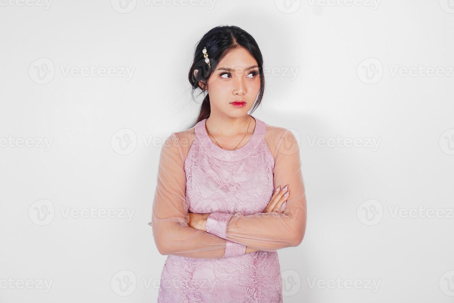 un asiatique Jeune femme portant rose robe est donnant sérieux expression tandis que traversée sa mains photo