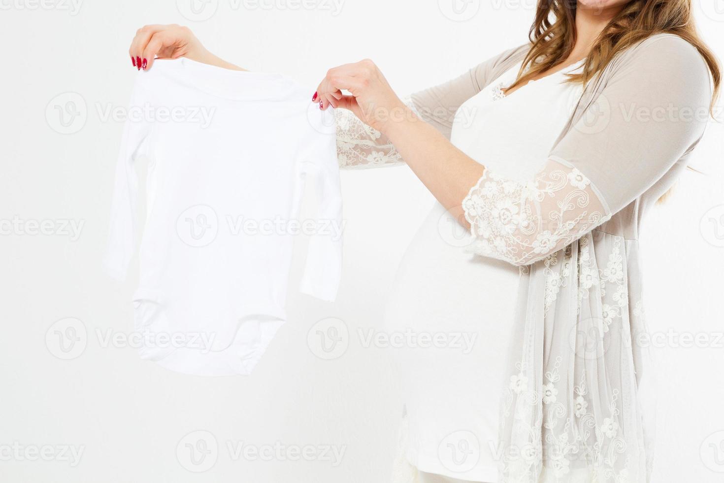 Femme enceinte tenant des vêtements pour nouveau-nés sur fond blanc Espace copie Espace heureux Naissance d'un enfant photo