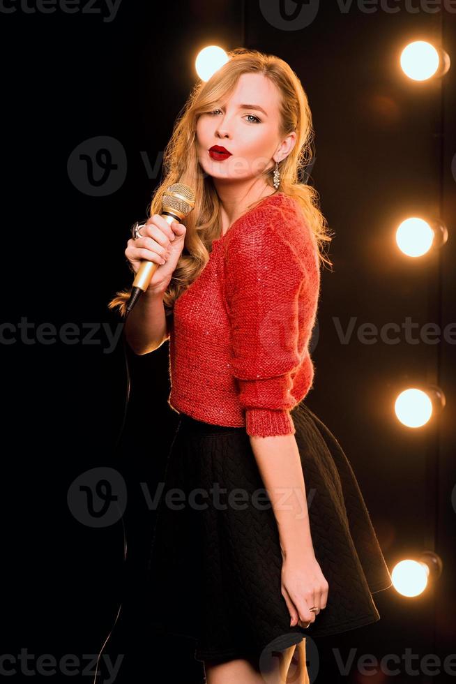 jeune smiley beaux cheveux longs en pull rouge fille avec microphone chantant une chanson sur la scène en karaoké photo