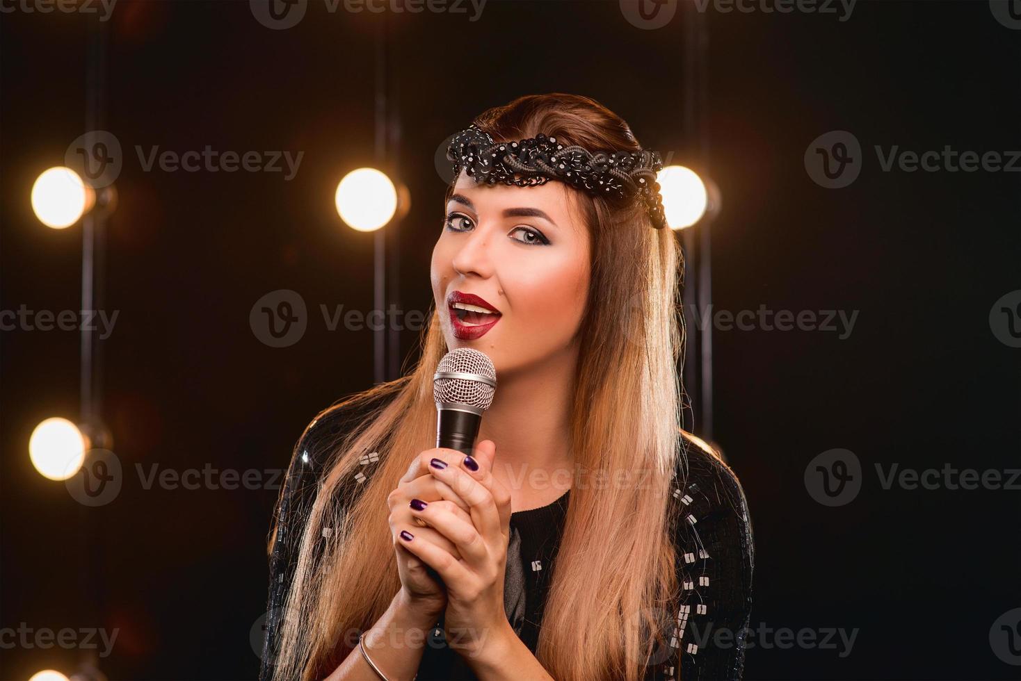 jeune smiley belle fille aux cheveux longs avec microphone chantant une chanson sur la scène en karaoké photo