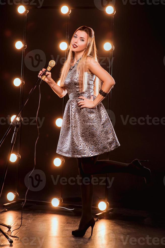 jeune smiley belle fille aux cheveux longs avec microphone chantant une chanson sur la scène en karaoké photo