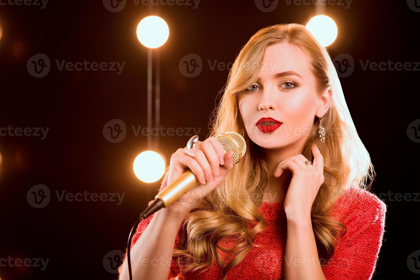 jeune smiley beaux cheveux longs en pull rouge fille avec microphone chantant une chanson sur la scène en karaoké photo