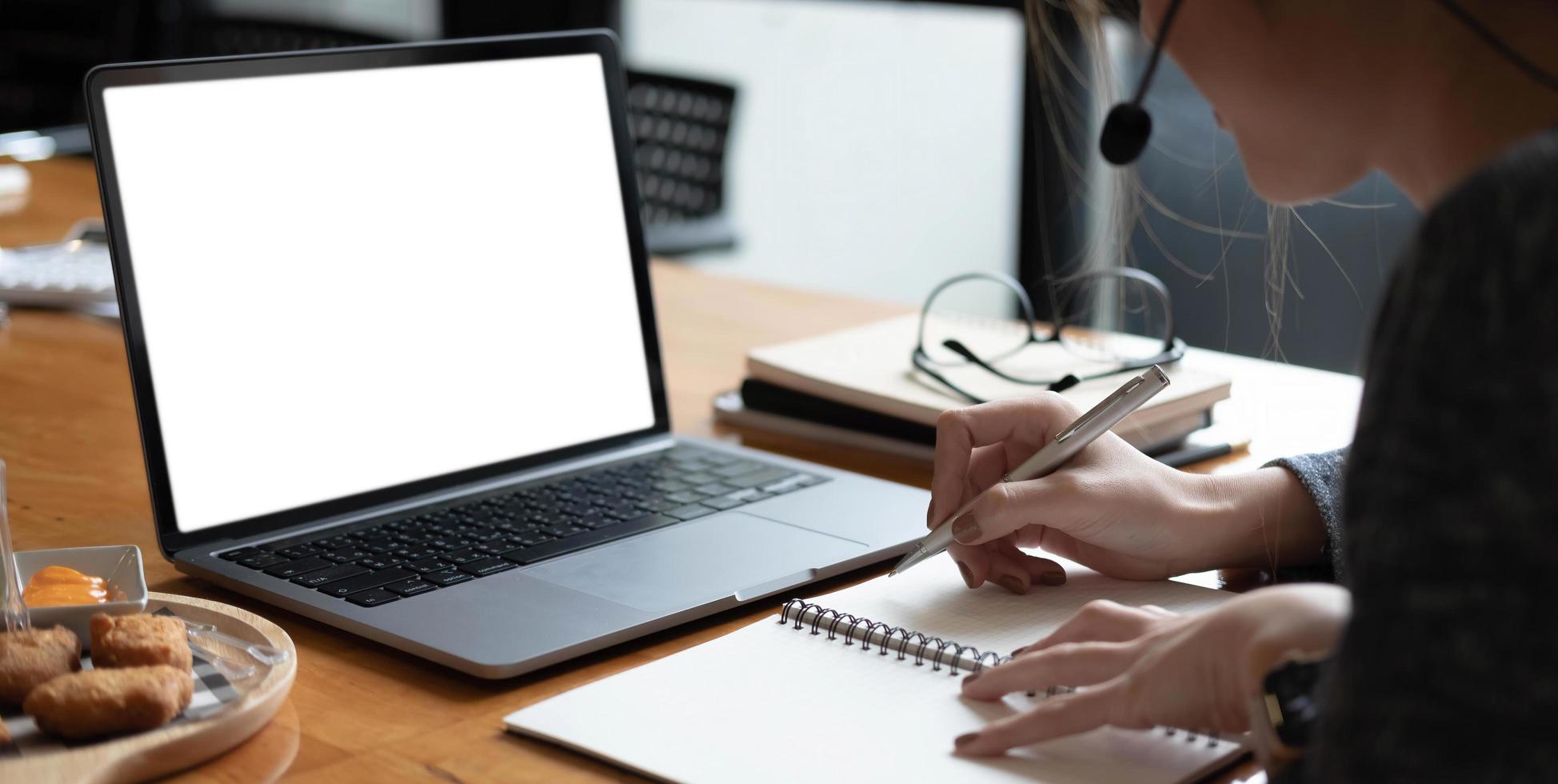 femme asiatique portant des écouteurs étudie en ligne en regardant un podcast de webinaire sur un écran vide d'ordinateur portable tout en travaillant photo