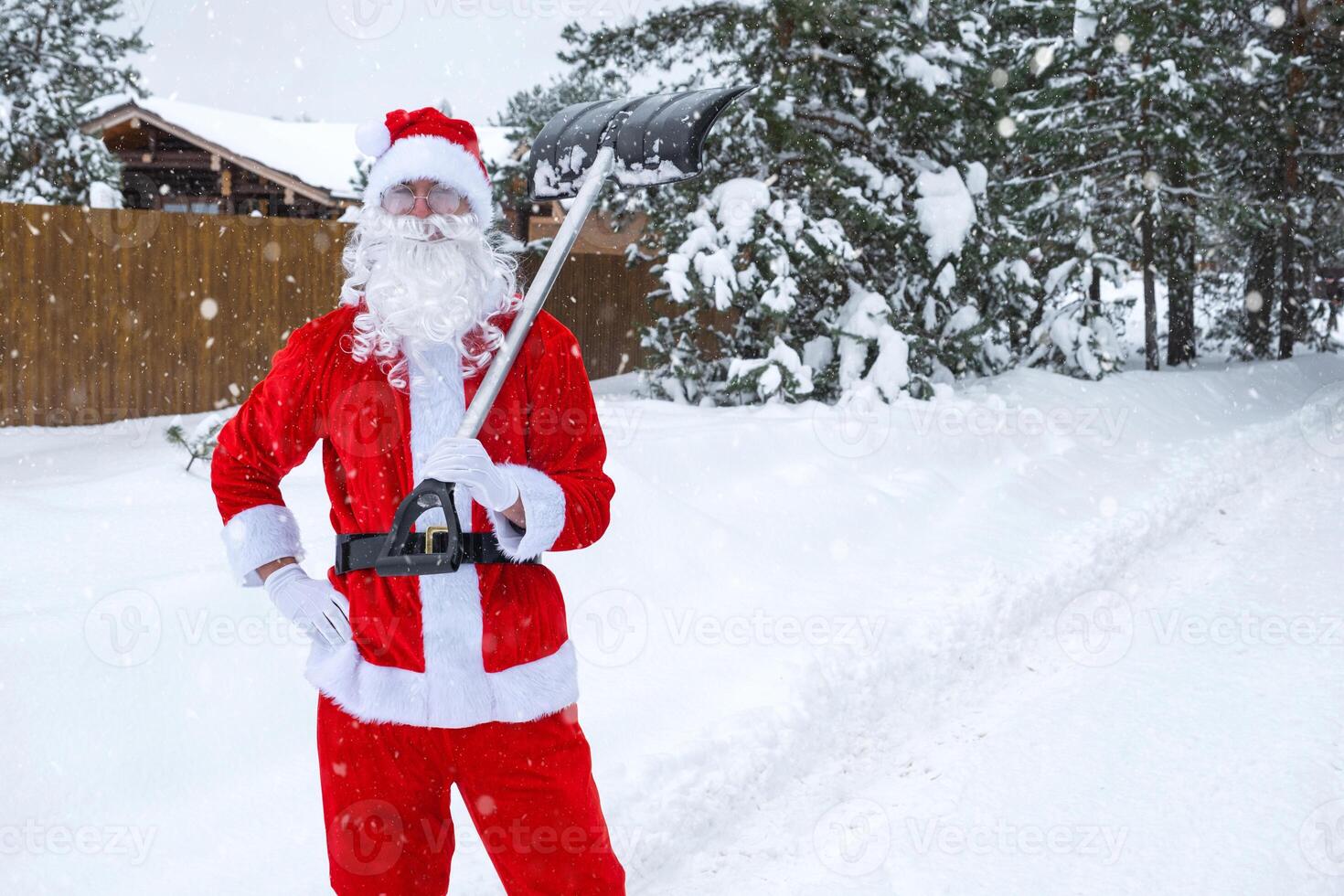 Père Noël claus nettoie neige avec pelle dans hiver en plein air après une chute de neige. nettoyage le des rues dans le village, clairière le passage pour voitures, difficile temps conditions pour Noël et Nouveau année photo