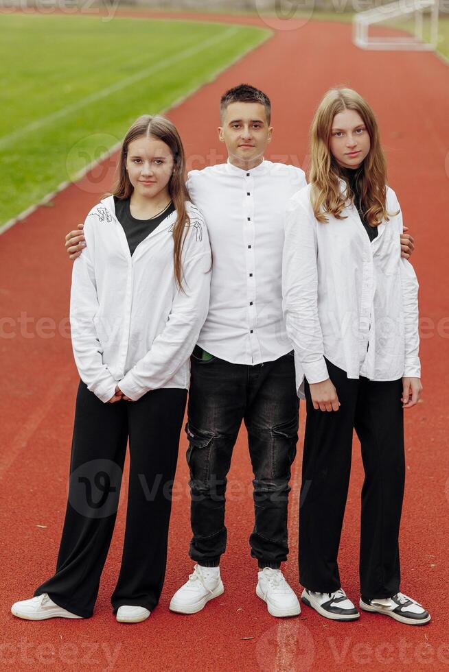 portrait de Trois adolescent dans décontractée vêtements séance dans une stade et posant à la recherche à le caméra. concept de amitié. une moment de Bonheur. photo