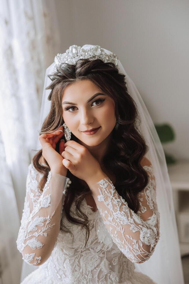 une magnifique magnifique portrait de une Jeune la mariée. magnifique la mariée avec mariage maquillage et bijoux couronne sur longue frisé cheveux. mariage photo modèle avec marron yeux dans une magnifique intérieur.