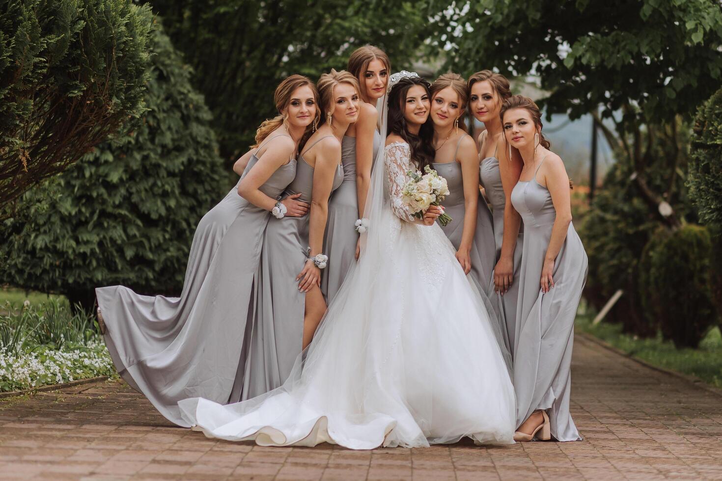 groupe portrait de le la mariée et demoiselles d'honneur. une la mariée dans une mariage robe et demoiselles d'honneur dans argent Robes tenir élégant bouquets sur leur mariage journée. photo