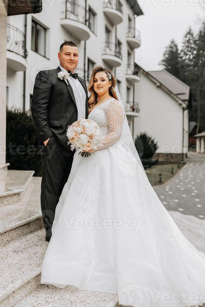 le la mariée et jeune marié sont en marchant près le Hôtel et poser, content et profiter le jour, en portant mains. une longue train sur le robe. hiver mariage photo