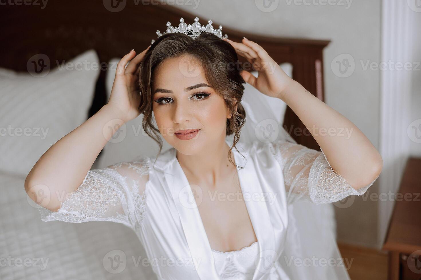 une magnifique brunette la mariée avec une tiare dans sa cheveux est avoir prêt pour le mariage dans une magnifique peignoir dans boudoir style. fermer mariage portrait, photo. photo