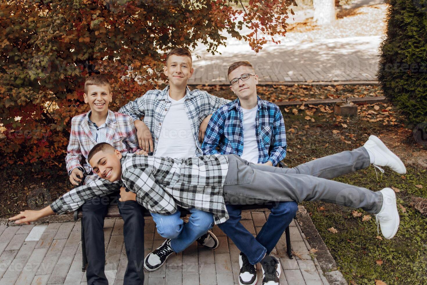 quatre adolescents sont ayant amusement et étant content tandis que séance sur une parc banc. adolescent camarades de classe sont repos contre le Contexte de l'automne la nature. photo