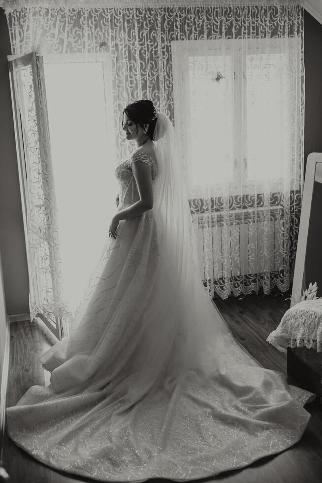 une luxueux la mariée avec une magnifique coiffure et une magnifique robe est avoir prêt pour le mariage la cérémonie dans le Matin. Matin photo de le la mariée à Accueil ou dans une Hôtel chambre. professionnel se maquiller.