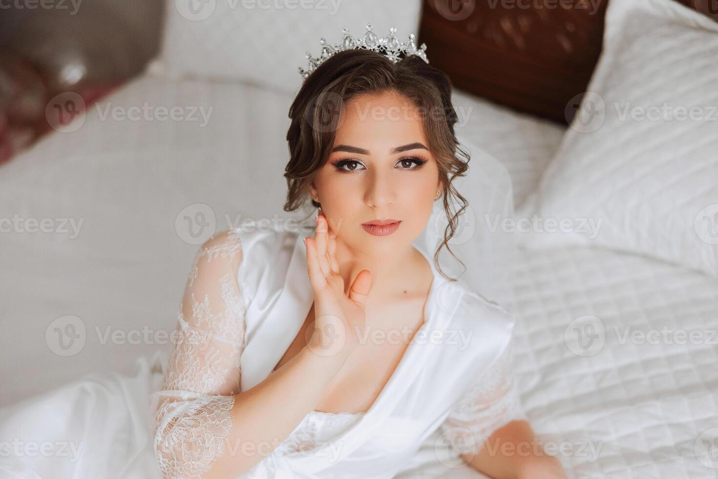 une magnifique brunette la mariée avec une tiare dans sa cheveux est avoir prêt pour le mariage dans une magnifique peignoir dans boudoir style. fermer mariage portrait, photo. photo