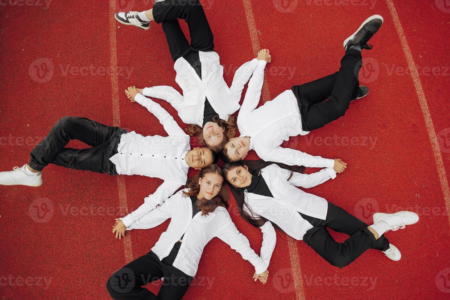 content copains mensonge ensemble dans une cercle à la recherche à le caméra, en portant mains et souriant tandis que mensonge sur une rouge mur... amitié, mode de vie, unité, affaires et travail en équipe concepts. photo