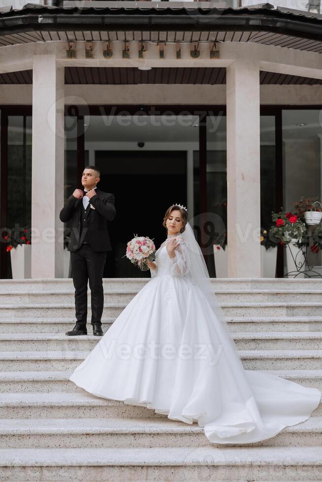 portrait de le jeunes mariés dans classique mariage vêtements sur une grand magnifique escalier. le concept de magasins et Ventes de des biens pour le la mariée et jeune marié. photo