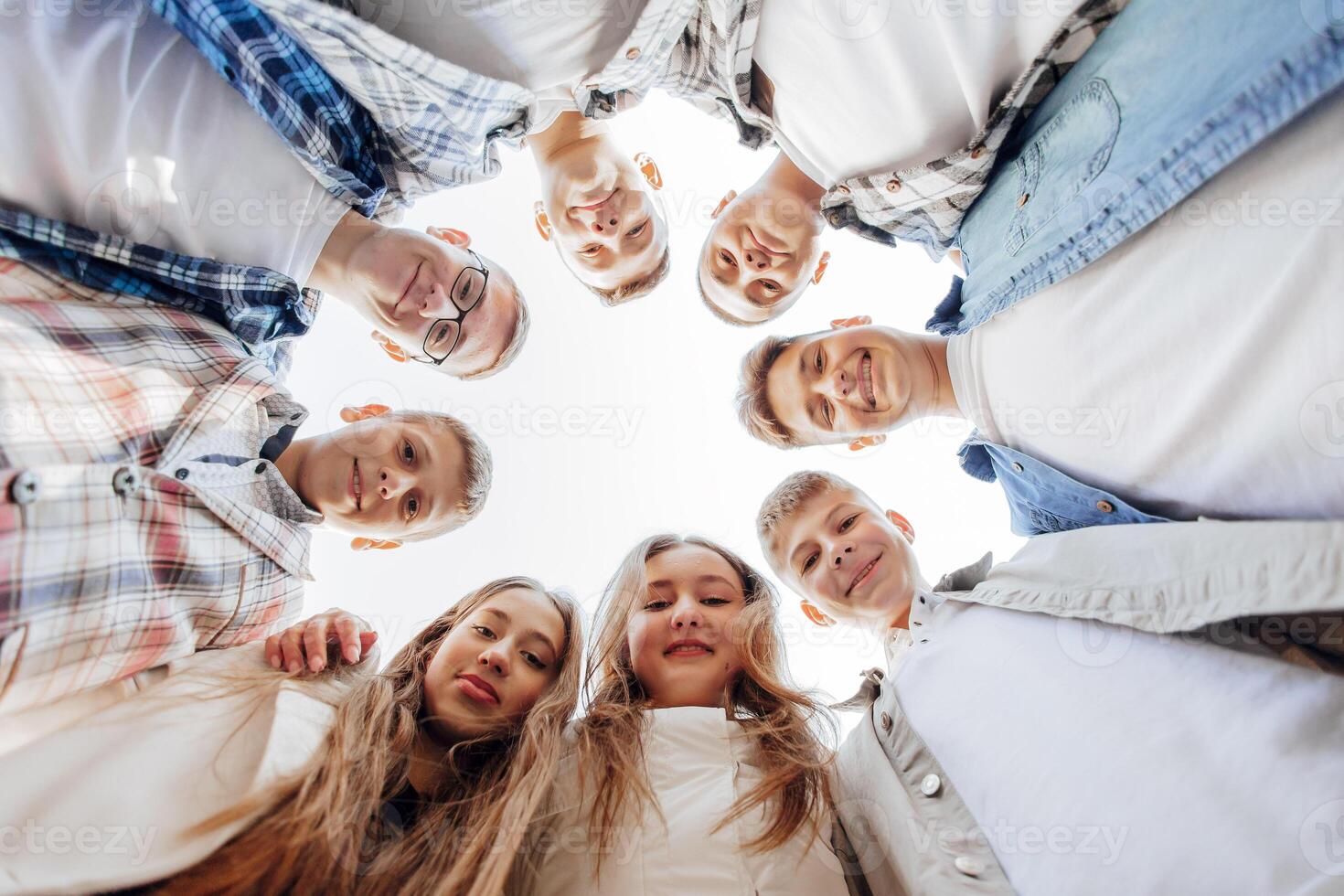 grand groupe de souriant Jeune gens debout, étreindre, à la recherche à caméra. groupe de de bonne humeur adolescent gens dans une cercle à la recherche bas. faible visualisation angle. copie espace. photo