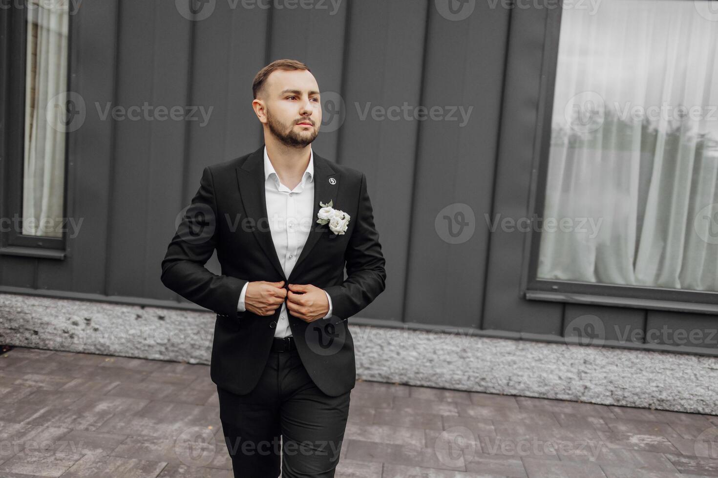 élégant et élégant jeune marié dans une noir costume et blanc chemise sur une foncé Contexte photo