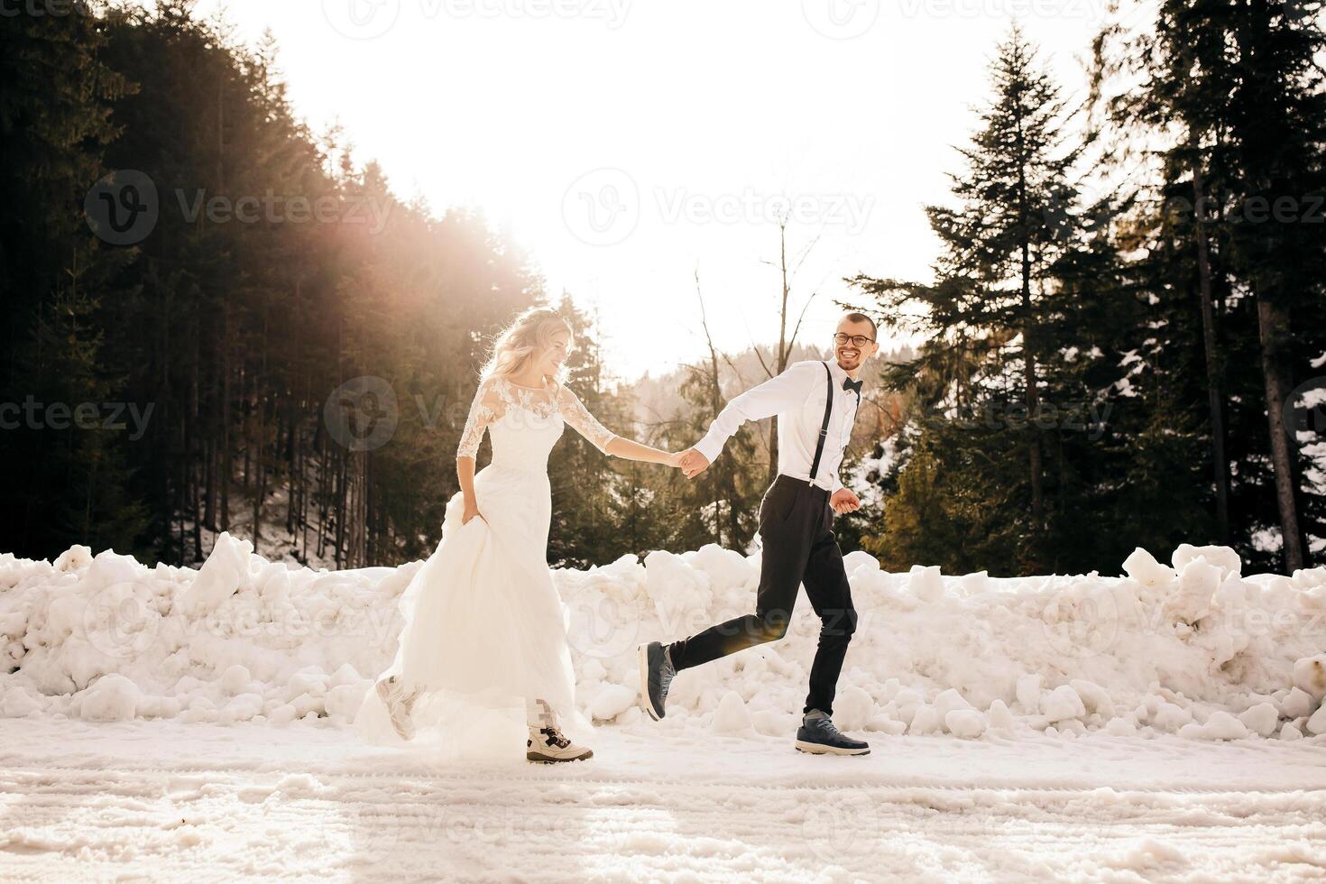 le la mariée et jeune marié sont fonctionnement le long de une neigeux route contre le Contexte de une pin forêt et magnifique contraste lumière du soleil. côté voir. hiver mariage. endroit pour logo. photo