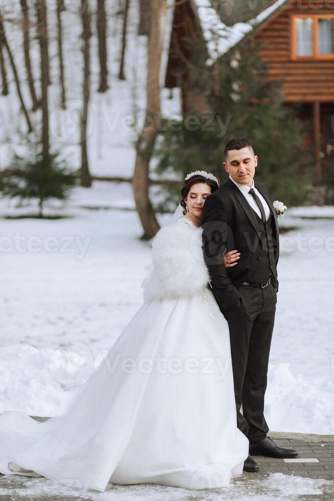 hiver mariage. content couple en marchant dans mariage vêtements étreindre et souriant dans une hiver parc couvert avec neige sur leur mariage journée. hiver l'amour récit de une magnifique couple dans neigeux hiver temps photo