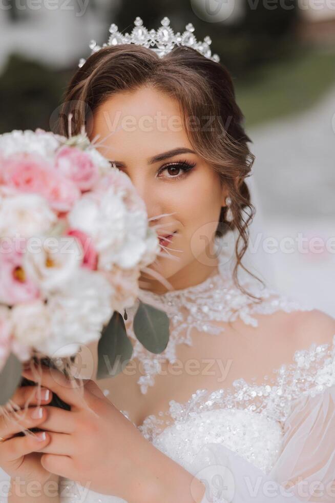 brunette la mariée dans hors de l'épaule dentelle blanc robe et tiare posant avec une bouquet de blanc et rose fleurs. magnifique cheveux et se maquiller. printemps mariage photo