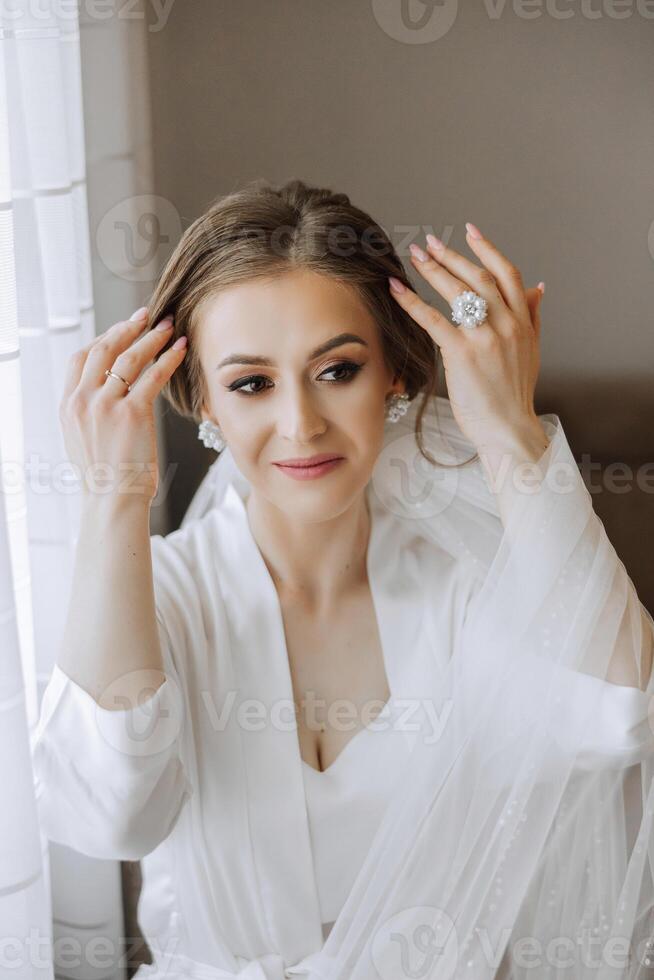 une magnifique brunette la mariée avec une tiare dans sa cheveux est avoir prêt pour le mariage dans une magnifique peignoir dans boudoir style. fermer mariage portrait, photo. photo