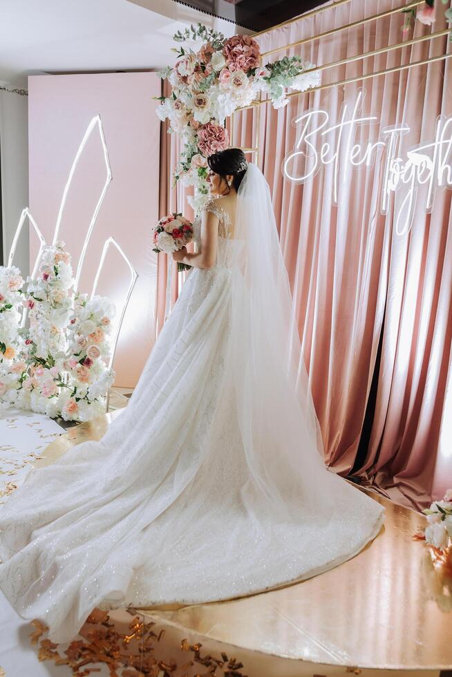 une brunette la mariée dans une tiare pose avec une bouquet de blanc et rose fleurs. magnifique cheveux et se maquiller. printemps mariage photo