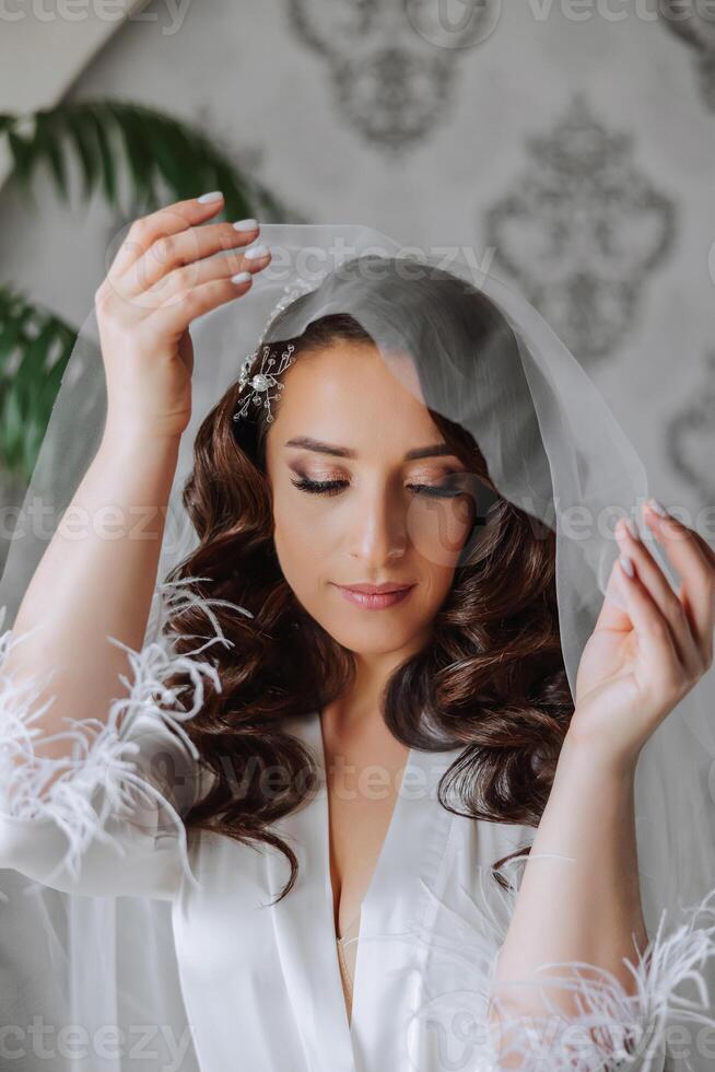 une magnifique brunette la mariée avec une tiare dans sa cheveux est avoir prêt pour le mariage dans une magnifique peignoir dans boudoir style. fermer mariage portrait, photo. photo