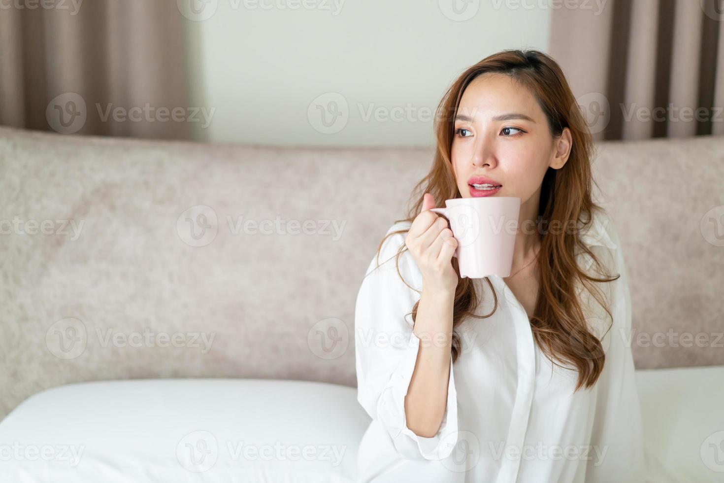 portrait belle femme se réveiller et tenant une tasse de café ou une tasse sur le lit photo