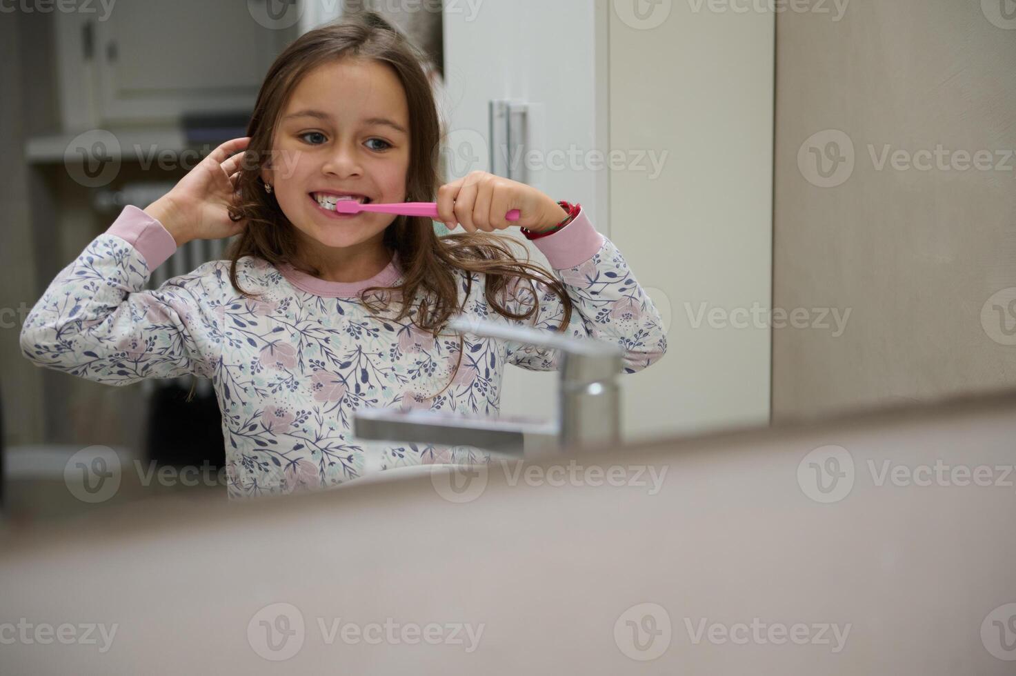 réflexion dans le salle de bains miroir de une mignonne enfant fille brossage dents, habillé dans pyjamas. dentaire hygiène et oral se soucier photo