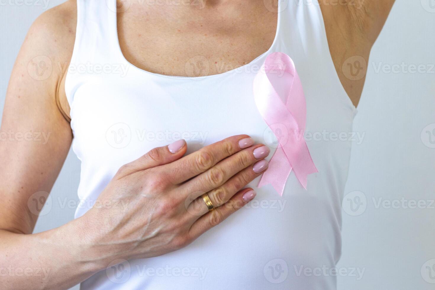 coup de le femme contre le blanc mur dans le blanc Haut avec rose ruban, comme une symbole de une Sein cancer conscience, performant soi examen de le seins, à la recherche pour anomalies. concept photo