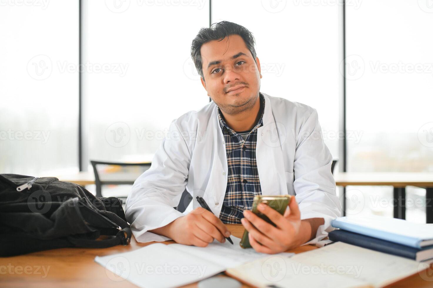 portrait de une Jeune Indien Masculin médical étudiant dans une blanc manteau agitant photo