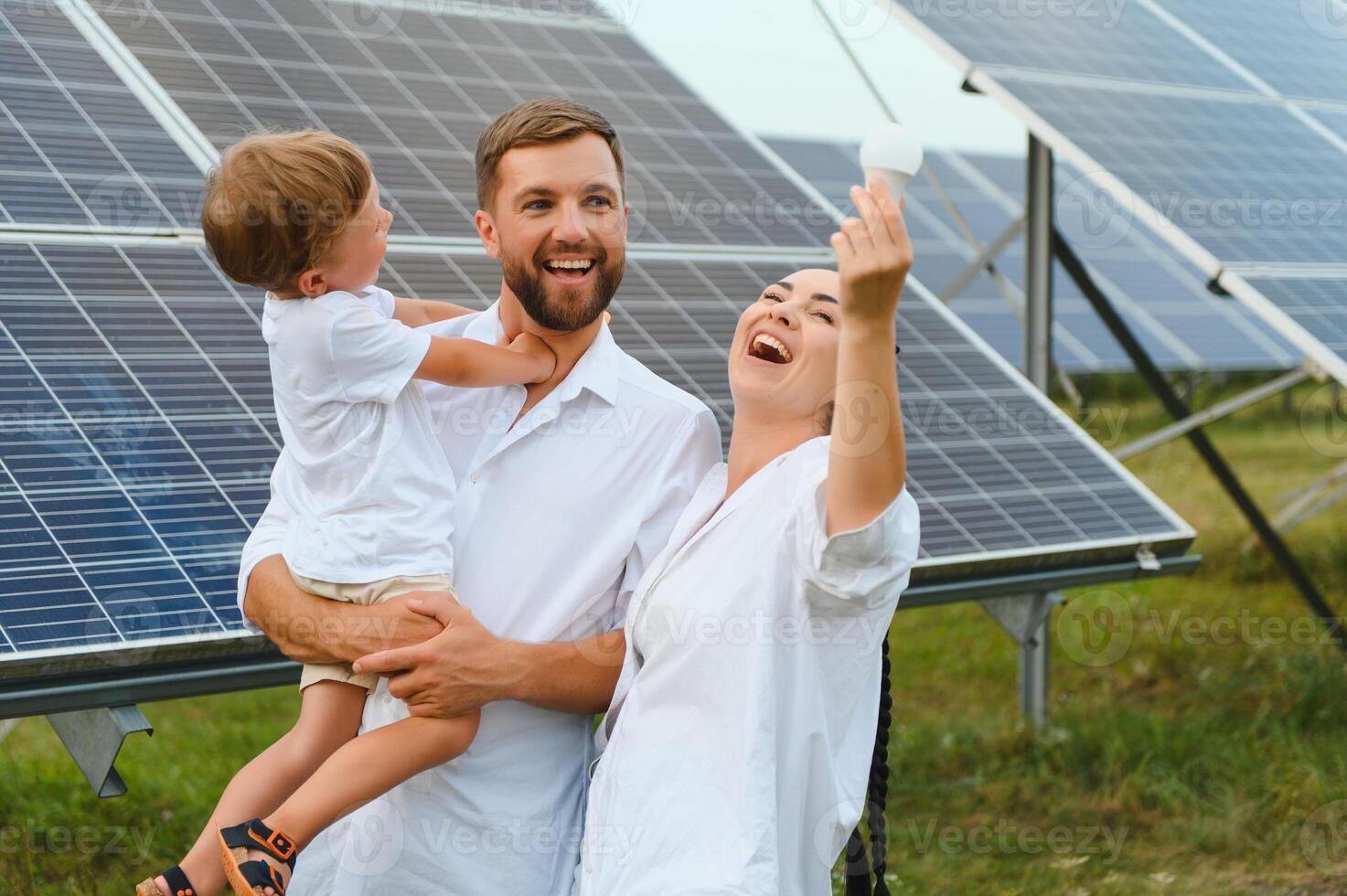 solaire énergie concept. une jeune, content famille est permanent près solaire panneaux et en portant un électrique lumière ampoule. photo