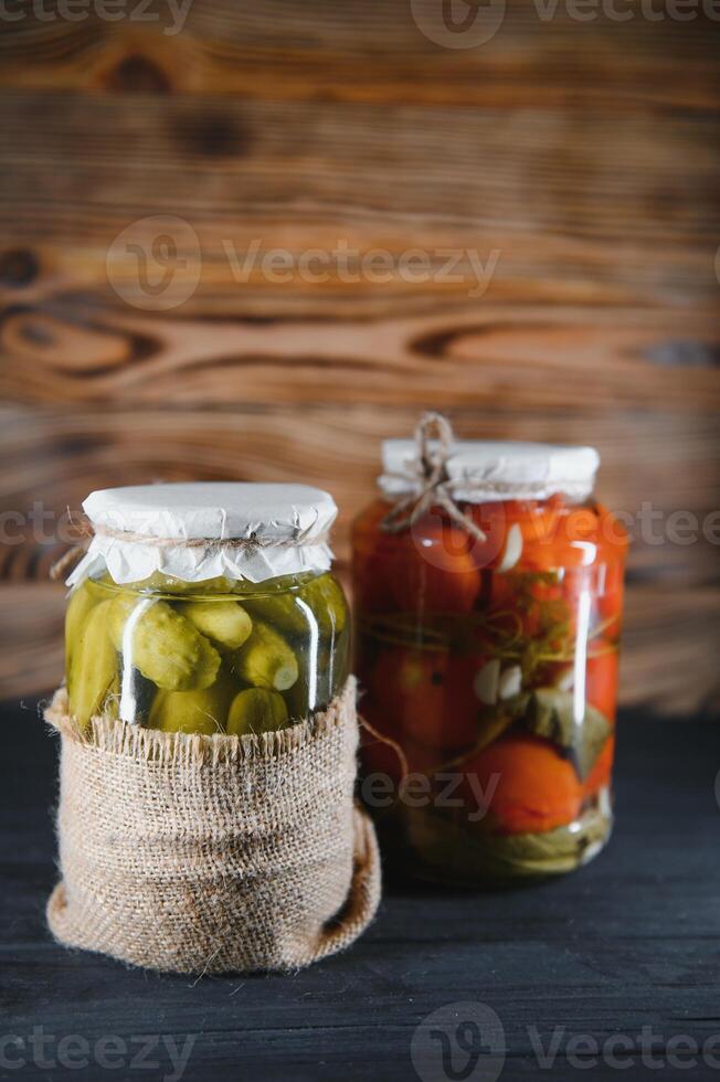 en conserve concombres et tomates avec artisanat couvercles sur une en bois Contexte. concombres et tomates avec endroit pour texte. les stocks de en conserve aliments. récolte, les stocks pour le l'hiver. photo