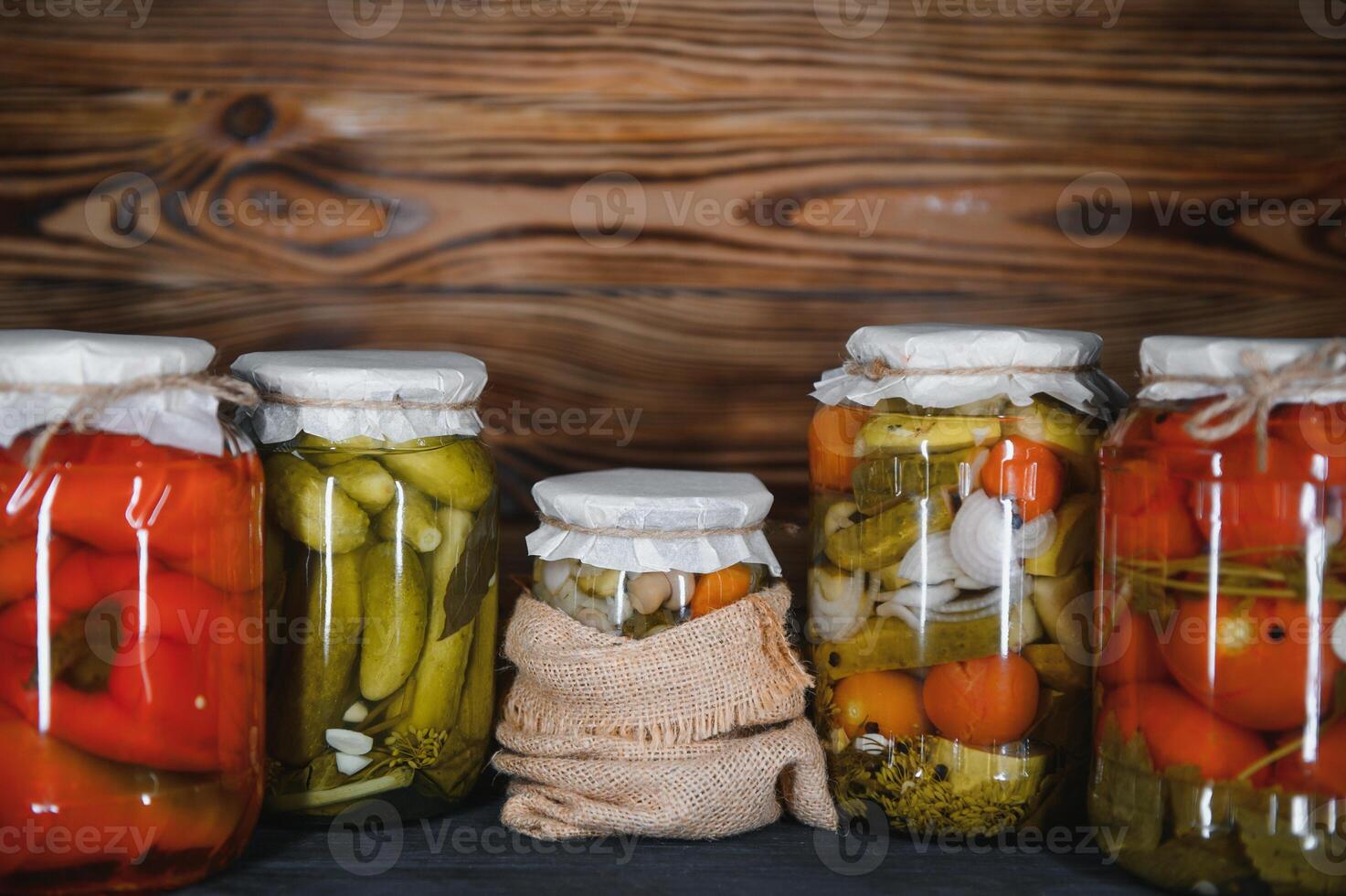 en conserve concombres et tomates avec artisanat couvercles sur une en bois Contexte. concombres et tomates avec endroit pour texte. les stocks de en conserve aliments. récolte, les stocks pour le l'hiver. photo