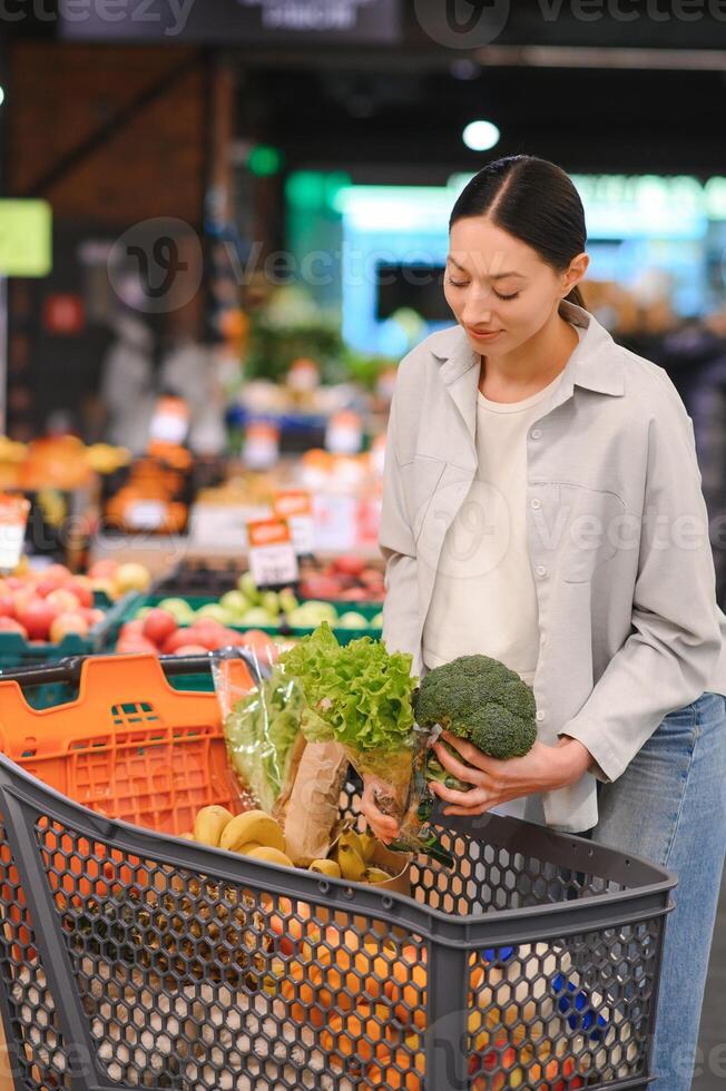 Jeune femme choisit brocoli, achat des légumes dans supermarché. photo