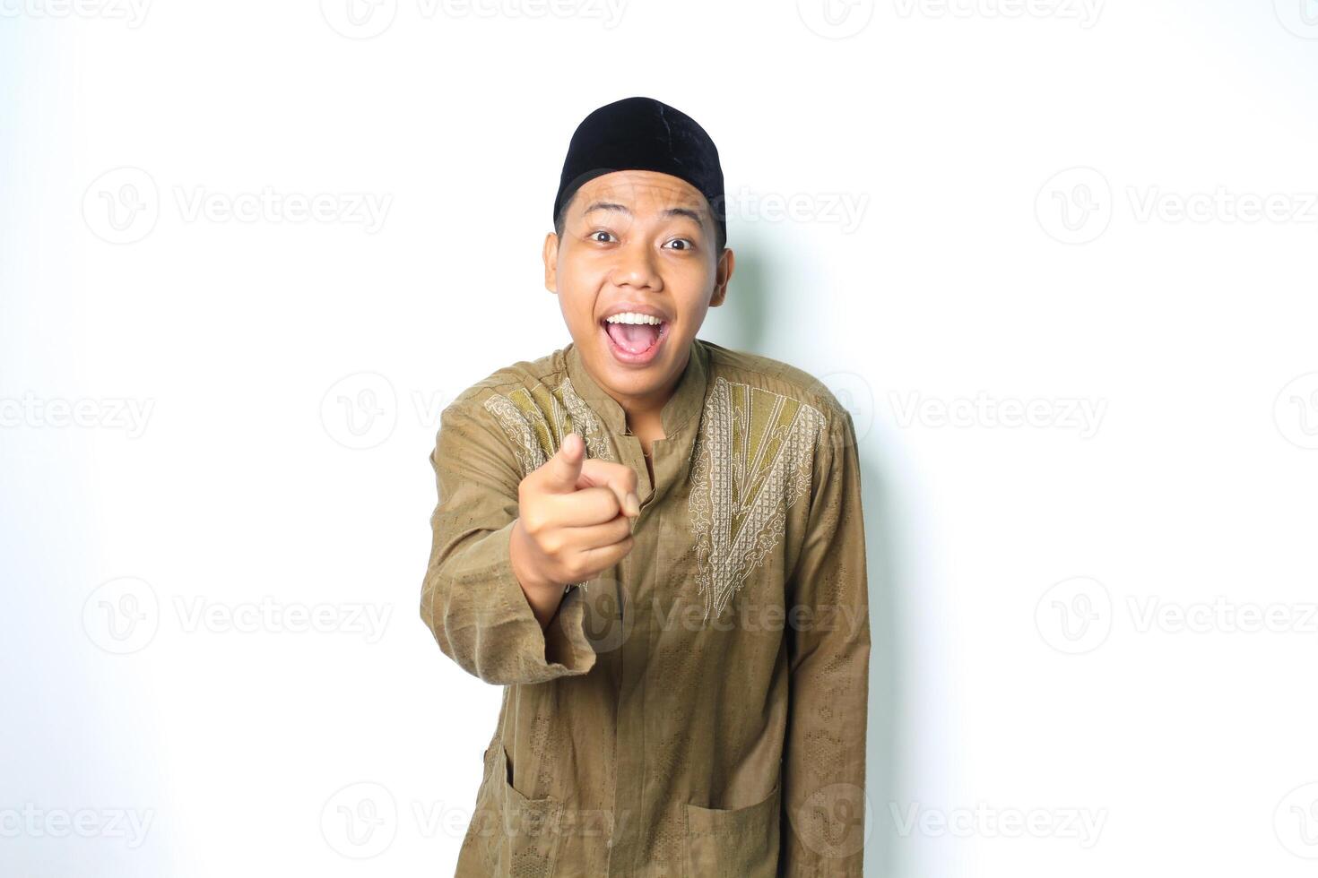 surpris asiatique musulman homme portant islamique vêtements montrer du doigt à caméra isolé dans blanc Contexte photo