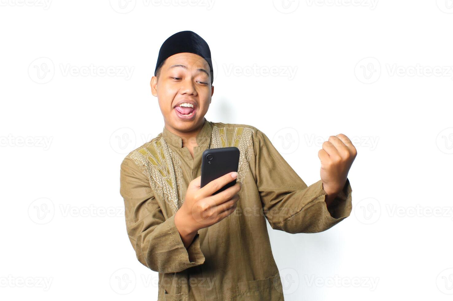 joyeux asiatique musulman homme portant islamique robe spectacle gagnant geste avec en portant mobile téléphone isolé sur pourquoi Contexte photo