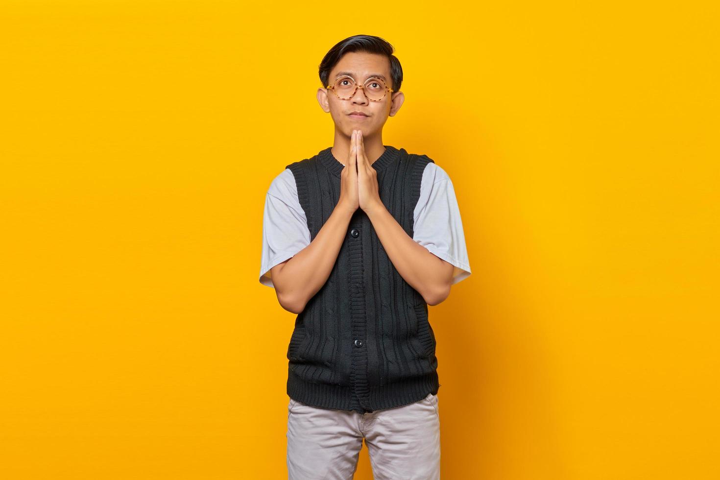 portrait de tristesse jeune homme asiatique montrant un geste de prière sur fond jaune photo