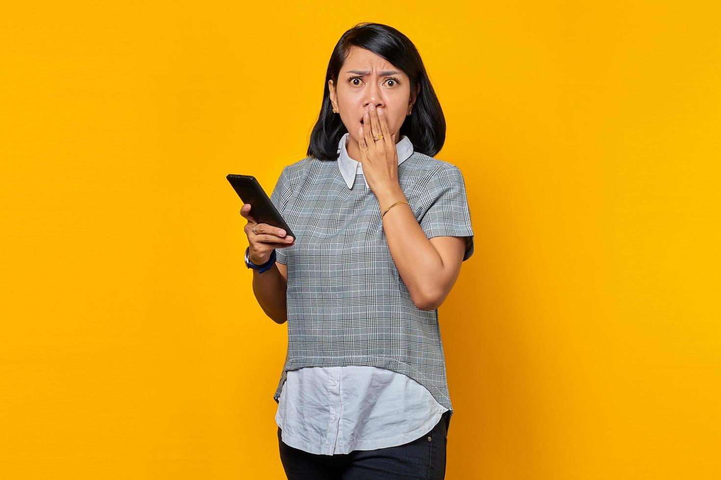 portrait d'une jeune femme asiatique choquée tenant un smartphone et couvrant la bouche avec la main photo