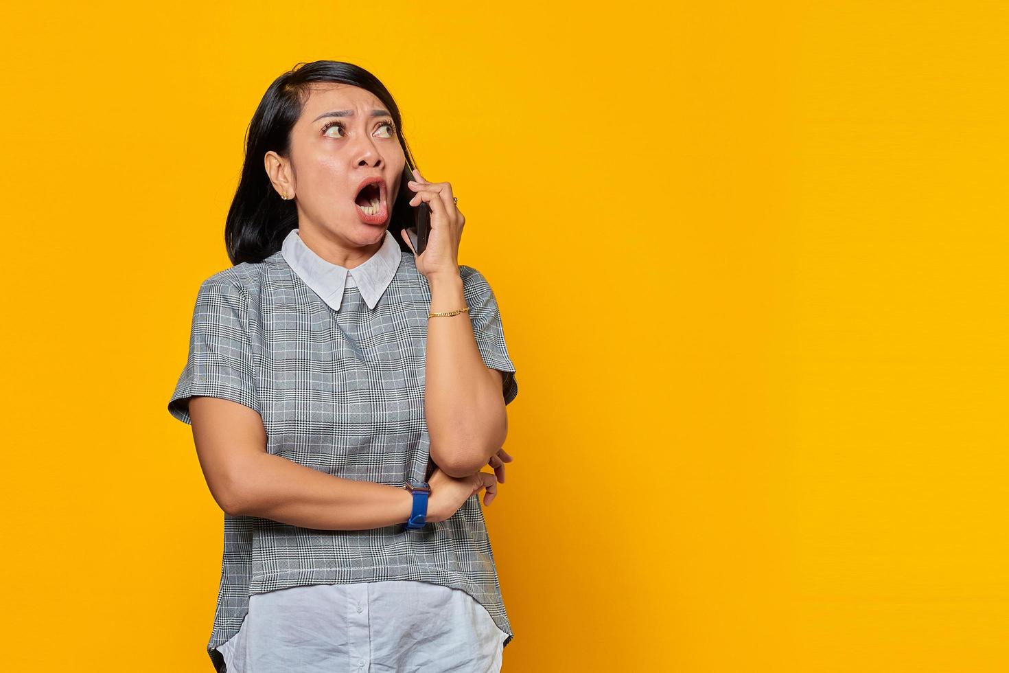 portrait d'une jeune femme asiatique choquée lors de la réception d'un appel entrant sur un smartphone sur fond jaune photo