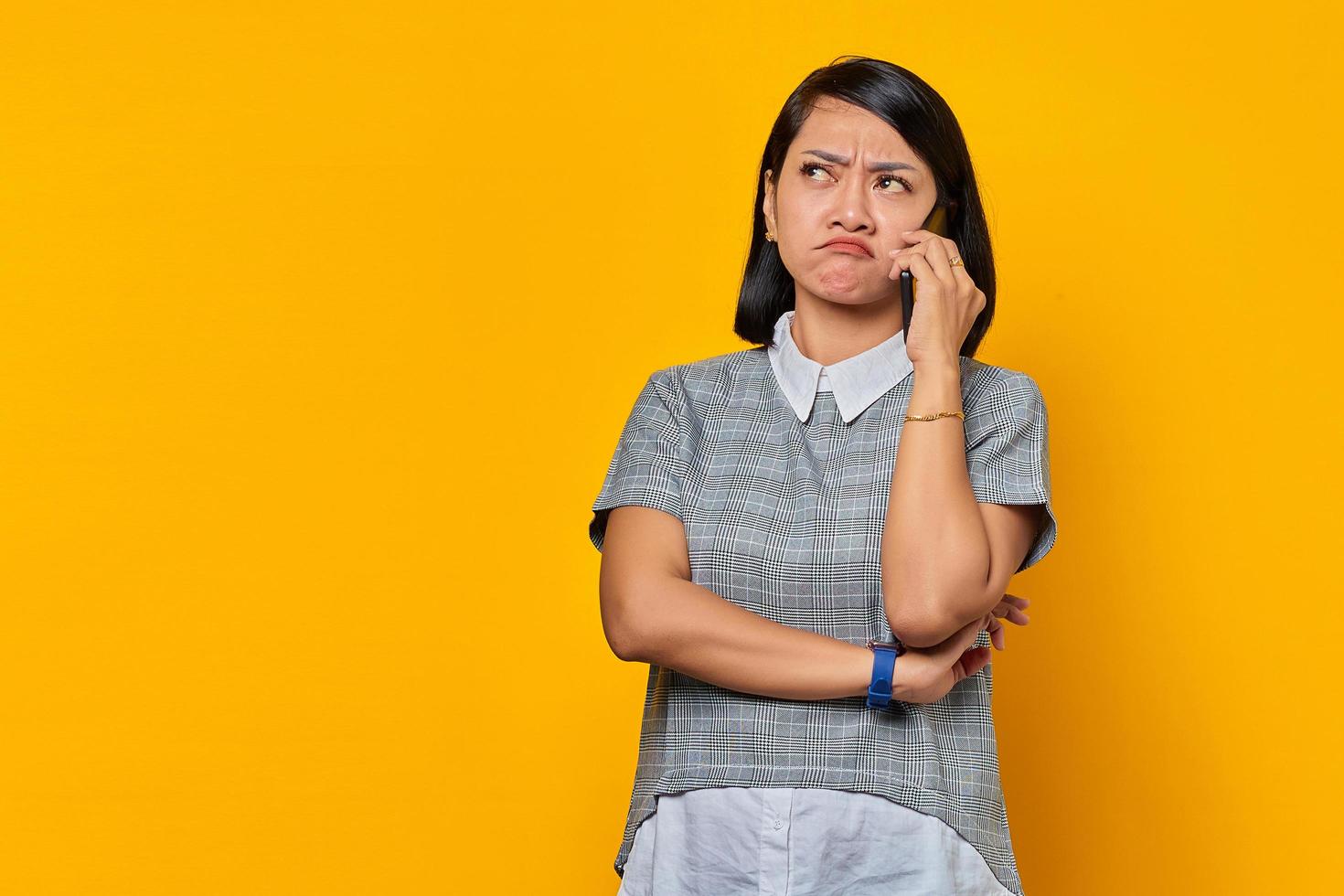 Portrait d'une jeune femme asiatique agacée recevant un appel entrant sur un smartphone et regardant de côté sur fond jaune photo