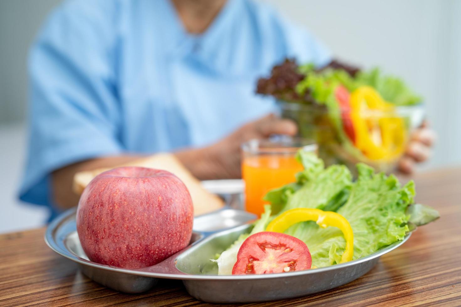 Une patiente asiatique âgée ou âgée de vieille dame mangeant un petit-déjeuner de légumes sains avec espoir et heureuse assise et affamée sur son lit à l'hôpital. photo