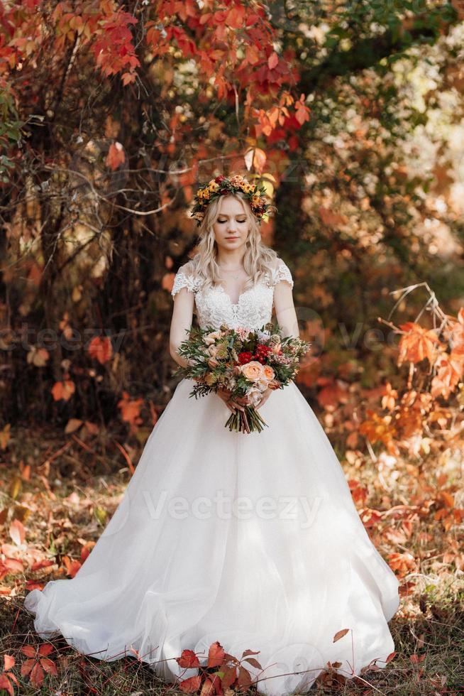 fille blonde dans une robe de mariée dans la forêt d'automne photo