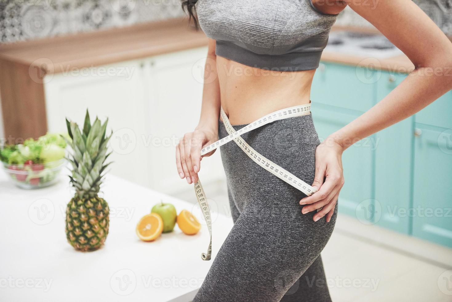 portrait d'une femme mesurant son corps mince sur un fond de cuisine. concept de remise en forme et de mode de vie sain photo