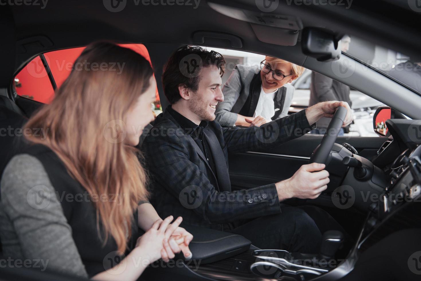 prendre leur décision. beau couple d'amoureux assis dans une nouvelle voiture ensemble chez le concessionnaire bel homme et sa petite amie aimante choisissant une voiture ensemble véhicule de consommation photo