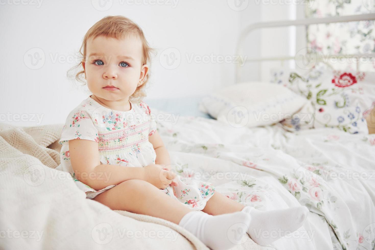 petite fille en robe mignonne implantation au lit jouant avec des jouets à la maison. chambre d'enfant vintage blanche. concept d'enfance photo