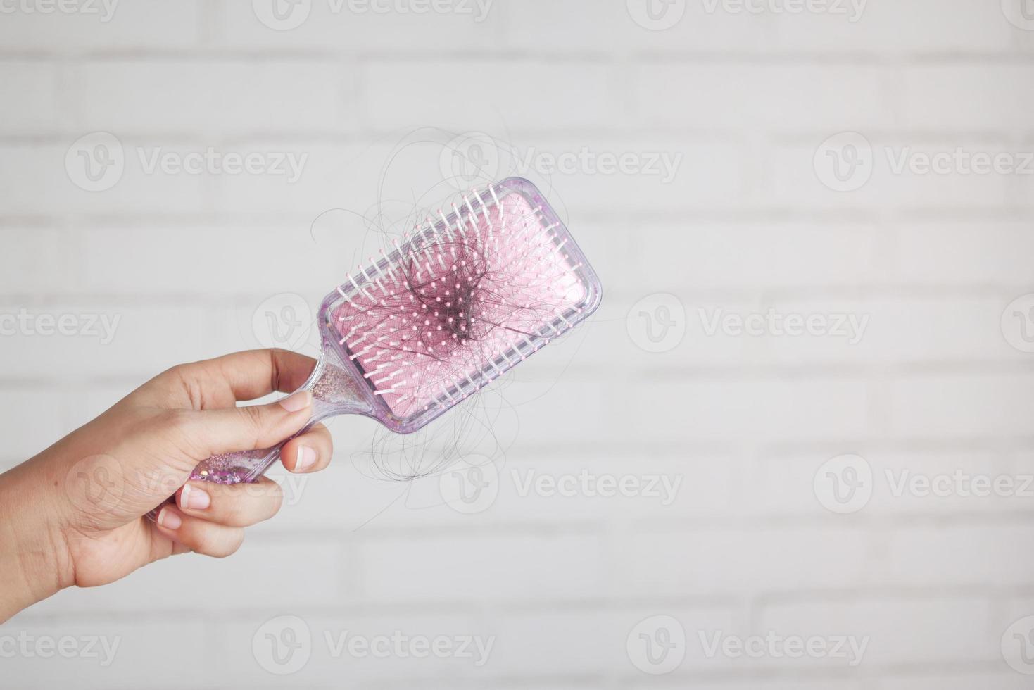 les femmes tiennent une brosse avec des cheveux perdus contre un mur blanc photo