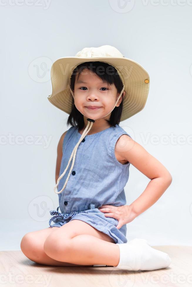 image verticale d'une jolie fille âgée de 4 à 5 ans assise dans une pose pliée, un enfant portant un chapeau de couleur crème pour l'aventure. photo